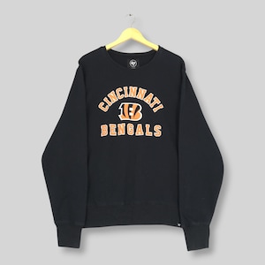 May include: A black long-sleeve crewneck sweatshirt featuring the text CINCINNATI BENGALS in orange block lettering with a white outline. The center graphic includes a stylized orange and black tiger stripe B logo. A small 47 brand tag is visible.