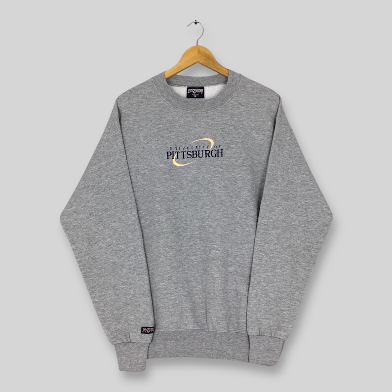 May include: A heather gray sweatshirt with the text "UNIVERSITY of PITTSBURGH" in gold and navy blue. The long-sleeved crew neck top has a small logo on the left cuff and a tag at the neckline.