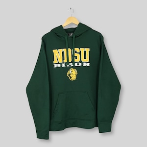 Può includere: Una felpa con cappuccio verde scuro con tasca a marsupio e cappuccio con coulisse. La parte anteriore presenta la scritta "NDSU BISON" in lettere gialle e bianche, con un logo del bisonte sottostante. La felpa è appesa a una gruccia di legno.