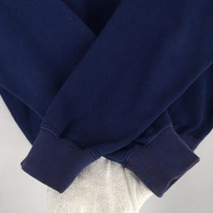 May include: Close-up of a navy blue sweatshirt with ribbed cuffs. The sleeves are folded over each other, showcasing the texture and colour of the fabric. The cuffs are a darker shade of navy blue.