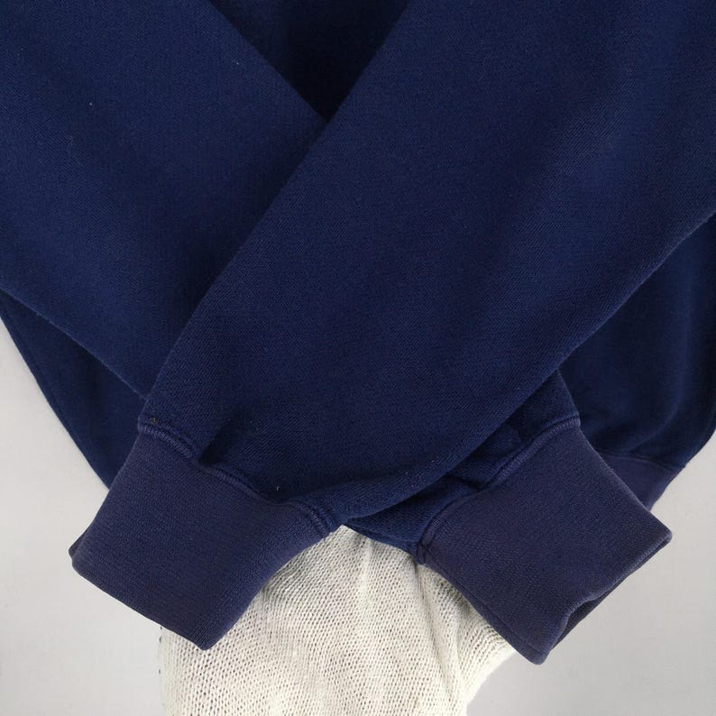 May include: Close-up of a navy blue sweatshirt with ribbed cuffs. The sleeves are folded over each other, showcasing the texture and colour of the fabric. The cuffs are a darker shade of navy blue.