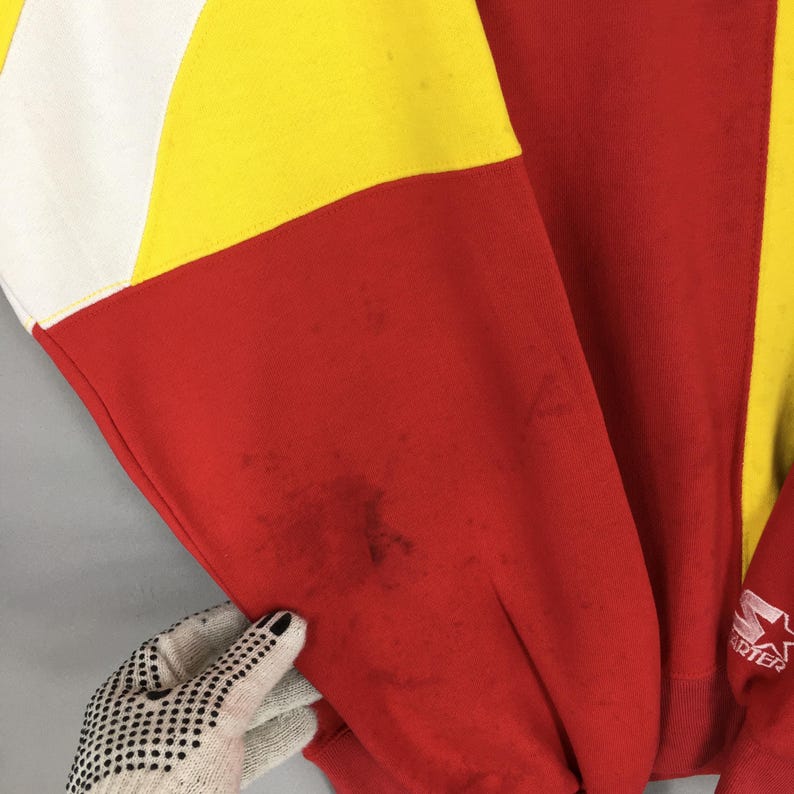 May include: A vintage red, yellow, and white color-block sweatshirt. The sleeve is red with a yellow and white section. The Starter logo is visible on the sleeve. The sweatshirt shows signs of wear with some stains.