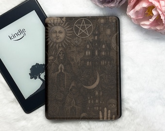 May include: A Kindle e-reader next to a dark brown cover with a gothic illustration. The cover features a sun, a pentagram, a haunted house, a crescent moon, and figures in cloaks. The Kindle screen displays the Kindle logo and a tree.