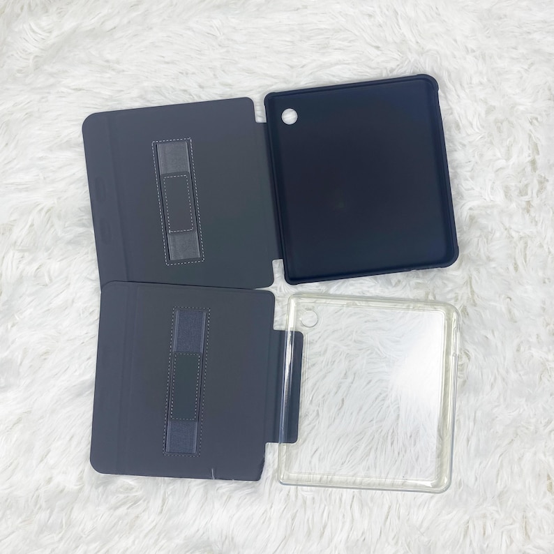 May include: Two tablet cases are displayed. One case is solid black with a dark grey interior featuring a vertical elastic strap. The second case is transparent with a black frame and a matching dark grey interior flap with a vertical elastic strap.