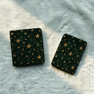 May include: Two rectangular cases with rounded corners, featuring a dark forest green background patterned with gold-colored stars of varying sizes and thin, delicate lines resembling shooting stars scattered across the surface.