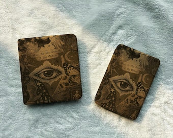May include: Two rectangular electronic reader covers featuring a dark brown and gold print with an eye, butterfly, ghost, skull, and moon. The text "Must be the Season of the Witch" is printed on both covers in a decorative font style.