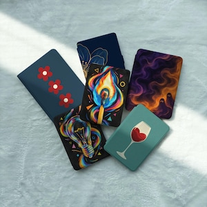 May include: A collection of six rectangular e-reader cases featuring diverse designs: three red flowers on blue, a gold floral outline on navy, a burning match, a lightbulb with colorful swirls, purple smoke with ghost shapes, and a wine glass.