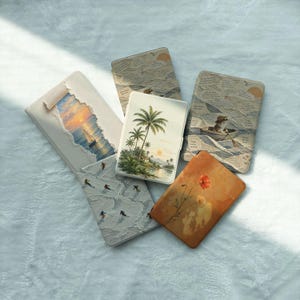 May include: Five rectangular e-reader cases featuring diverse designs: a sailboat at sunset, a collage of text, a tropical palm tree landscape, skiers on a snowy mountain, and a single orange poppy flower on a warm-toned background.