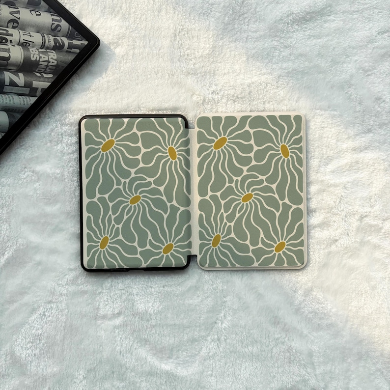 May include: A rectangular e-reader case featuring a repeating pattern of sage green wavy-petaled flowers with mustard yellow centres. The case is shown in an open position, displaying the interior design on both panels against a white textured surface.