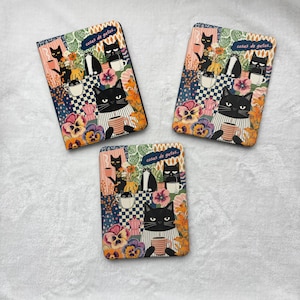 May include: Three rectangular e-reader covers featuring a repeating illustration of black cats drinking from mugs, surrounded by colourful flowers and checkered patterns. Each cover displays the text "cosas de gatos" in a small blue banner.
