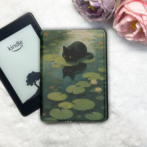 Op de afbeelding: Een zwarte Kindle e-reader naast een hoesje met een zwarte kat op waterlelies in een vijver. Het Kindle-scherm toont het Amazon-logo en een boom silhouet. De hoes heeft een illustratie in aquarel stijl.
