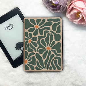 Op de afbeelding: Een Kindle e-reader met een bloemenpatroon hoes. De hoes heeft een groen en beige ontwerp met oranje accenten. Het Kindle-scherm toont het woord "kindle" en een boom silhouet.