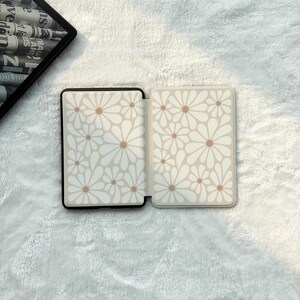 May include: A rectangular e-reader case featuring a repeating pattern of white daisy flowers with light brown centres on a cream background. The case is shown in an open position, displaying the interior and exterior panels with the floral design.