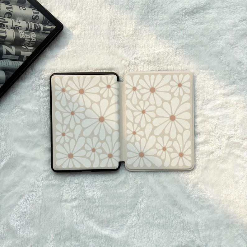 May include: A rectangular e-reader case featuring a repeating pattern of white daisy flowers with light brown centres on a cream background. The case is shown in an open position, displaying the interior and exterior panels with the floral design.