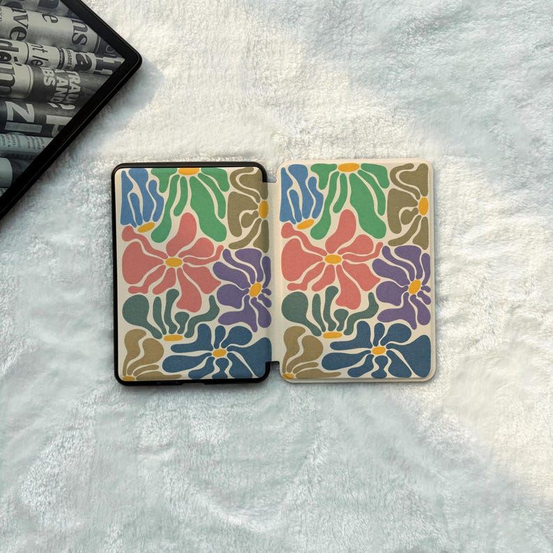 May include: A rectangular e-reader case featuring a repeating pattern of stylised flowers in shades of pink, blue, green, purple, and yellow. The case is shown in an open position, displaying the interior and exterior panels with a consistent floral design.