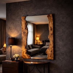 May include: A large rectangular mirror with a natural wood frame. The frame has a unique, organic shape with a light brown color. The mirror is hanging on a dark gray wall in a room with a lamp and a small table.