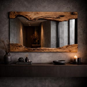 May include: A rectangular mirror with a natural wood frame. The frame has a live edge design, showcasing the wood's organic shape and texture. The mirror reflects a room with neutral tones and a warm ambiance. A dark wooden console table below the mirror holds decorative items.