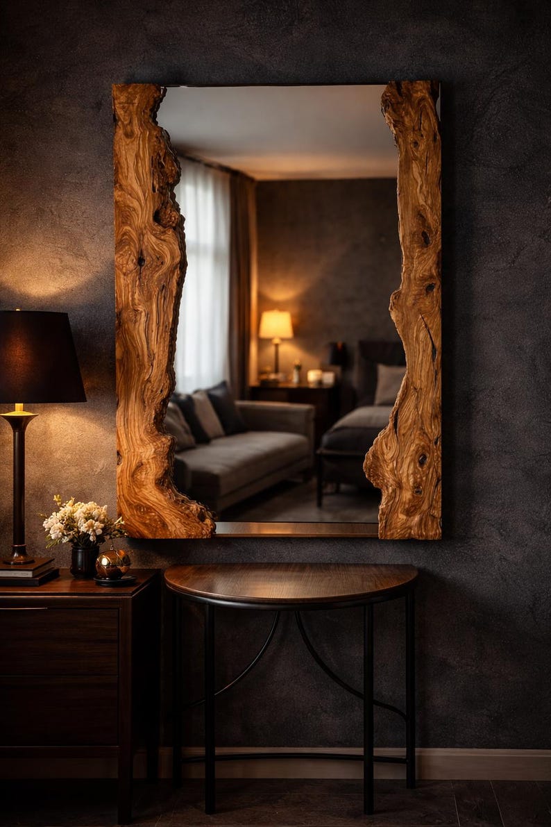 May include: A rectangular mirror with a natural wood frame. The frame has a raw, organic edge, showcasing the wood's texture and colour variations. The mirror hangs on a dark grey wall, reflecting a room with a sofa and lamps.