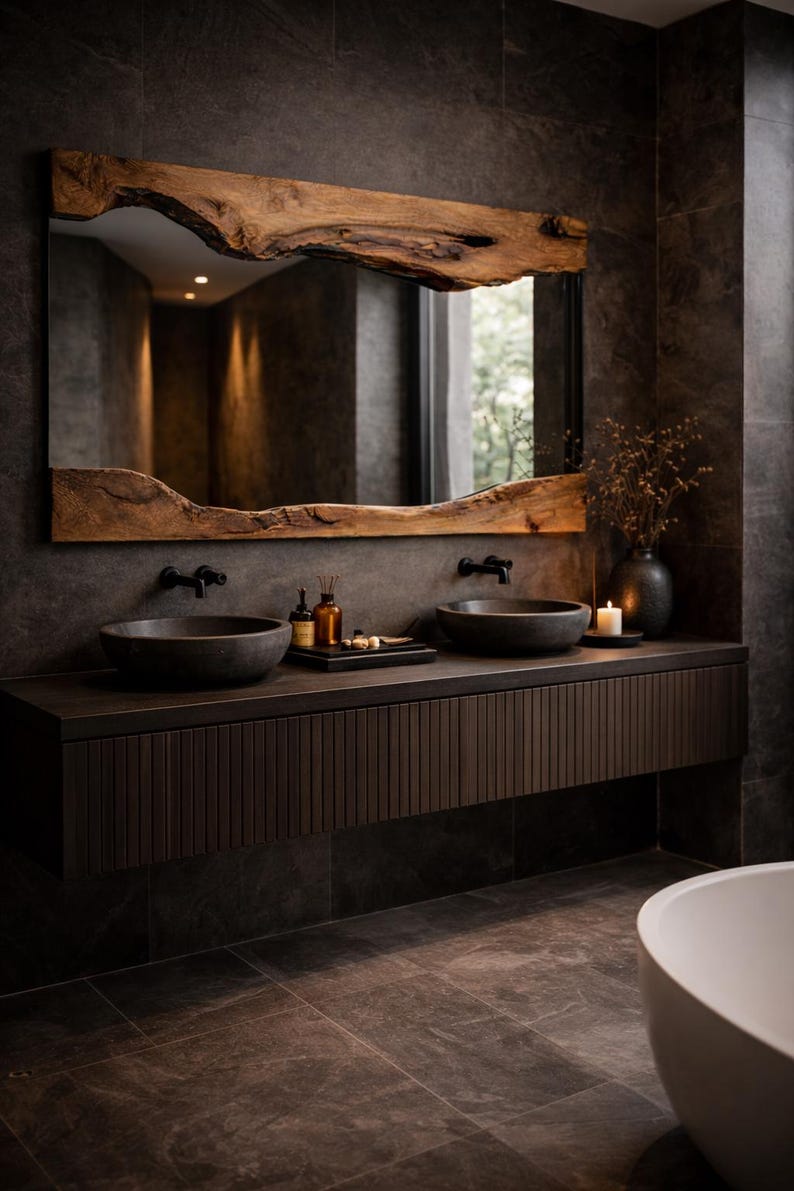 May include: A modern bathroom vanity with a large mirror framed by a natural wood slab. The dark wood vanity features two round sinks, black faucets, and a dark countertop. The walls and floor are dark gray tile.