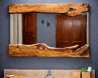 May include: Rectangular mirror with a natural wood frame. The frame has a raw, organic edge, showcasing the wood's grain and texture. The mirror is mounted on a dark blue wall above a bathroom sink.