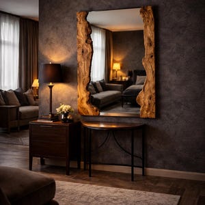 May include: A rectangular mirror with a wooden frame. The frame has an irregular, natural edge and a light brown hue. The mirror is mounted on a dark grey wall. A lamp and small table are visible in the room.