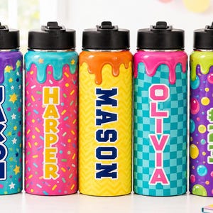May include: Five cylindrical metal water bottles with black lids and a decorative dripping paint design at the top. Each bottle features a unique pattern and a personalized name or number: JAXON, HARPER, MASON, OLIVIA, and #23 in bold letters.