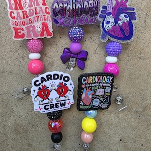 Puede incluir: Cinco portatarjetas con adornos acrílicos de temática médica. Los diseños incluyen textos como In My Cardiac Sonographer Era, Cardiology Crew, un corazón anatómico etiquetado, dos corazones de dibujos animados e iconos médicos.