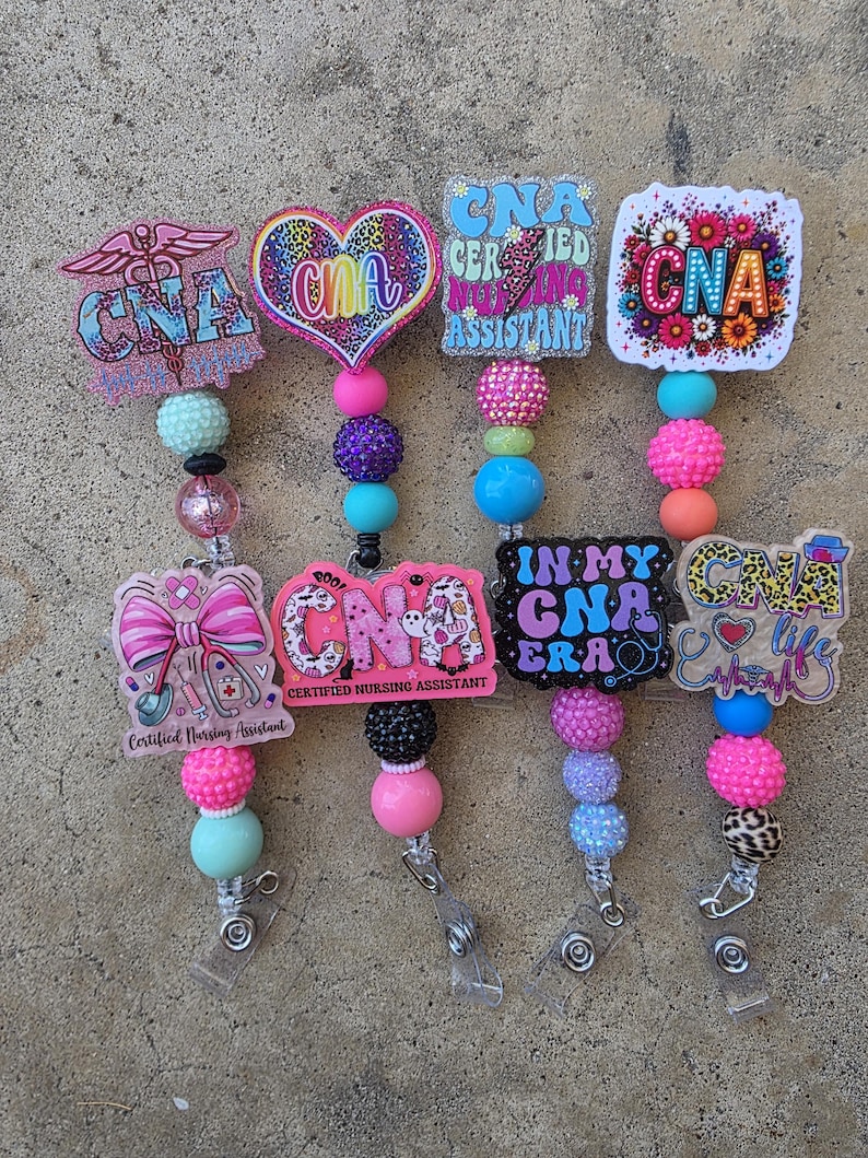 May include: Four badge reels featuring CNA designs with colorful acrylic toppers, including hearts, flowers, and medical symbols. Each reel has a beaded lanyard with various textures and colors, including pink, blue, purple, and leopard print, ending in a metal clip.