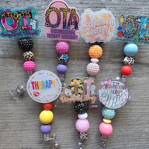 May include: A collection of six badge reels featuring occupational therapy themes. Each reel includes colorful acrylic toppers with text like OT, OTA, and Therapy Squad, attached to strands of multi-colored, textured, and patterned silicone beads.