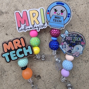 Può includere: Tre portabadge con decorazioni in acrilico a tema risonanza magnetica. Uno riporta MRI technologist, uno una macchina per risonanza con il testo MRI TECH, e uno in my MRI TECH era. Ogni portabadge ha perline colorate, testurizzate e lisce.