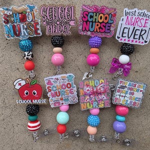 Puede incluir: Cuatro portatarjetas con adornos acrílicos coloridos con temas de enfermería escolar y textos como School Nurse y Best School Nurse Ever. Cada portatarjetas tiene un cordón con cuentas redondas de varios colores como azul, rosa, rojo y negro.