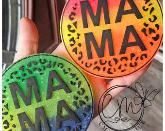 Könnte beinhalten: Zwei runde Untersetzer mit einem Regenbogen-Ombre-Design und einem schwarzen Leopardenmuster-Rand. Die Untersetzer haben das Wort "MAMA" in schwarzen Buchstaben.