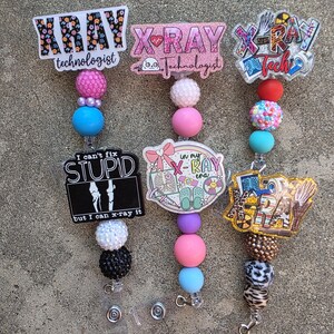 May include: Three badge reels featuring colorful beads and acrylic toppers. The toppers display text including XRAY technologist, I can't fix STUPID but I can x-ray it, in my X-RAY era, and X-RAY Tech, alongside medical and skeletal illustrations.