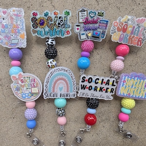 May include: A collection of seven badge reels featuring acrylic toppers with social worker themes, colorful beads, and metal clips. The designs include text such as Social Worker, In My Social Worker Era, and I'll Be There For You, alongside icons like rainbows, flowers, and office supplies.
