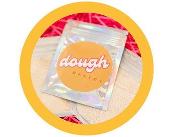 May include: A silver pouch with a holographic finish containing white sprinkles. The pouch has a yellow circle sticker with the text "dough bakery" in pink.