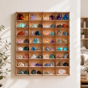 Puede incluir: Un expositor de madera con numerosas piedras preciosas pequeñas y coloridas. Las piedras preciosas están dispuestas en compartimentos individuales, mostrando una variedad de colores, incluyendo rojo, morado, azul, verde y amarillo. El expositor está montado en una pared blanca.