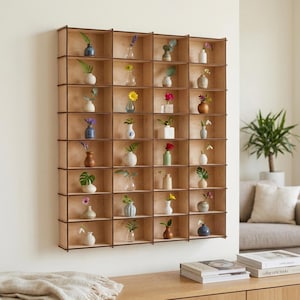 Puede incluir: Una estantería de pared de madera con numerosos compartimentos pequeños, cada uno con un jarrón en miniatura con una flor o planta. La estantería es de madera clara con ribetes marrones oscuros, creando un patrón de rejilla. Los jarrones son de varios colores y formas.
