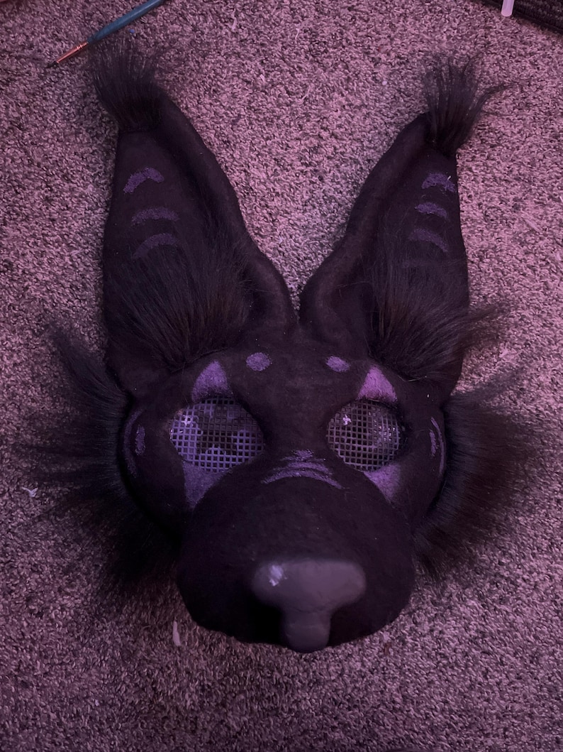 May include: A black furry mask with purple accents and mesh eyes. The mask has a pointed nose and large ears.