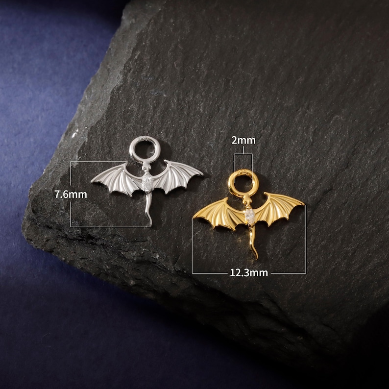 May include: Two dragon-shaped charms, one silver and one gold, each with a small gemstone. The silver charm is 7.6mm long, the gold charm 12.3mm. Both have a 2mm ring at the top for attachment. Ideal for jewellery making.