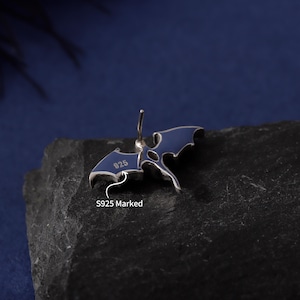 May include: A silver-colored earring with a blue enamel bat wing design. The earring is marked with "925" and "S925 Marked". The bat wings are spread out, and the earring has a post for piercing.