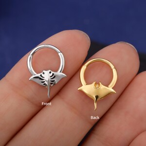 May include: Two hoop earrings, one silver and one gold, each featuring a manta ray design. The silver earring is labeled "Front" and the gold earring is labeled "Back". The earrings are shown against a blue background.
