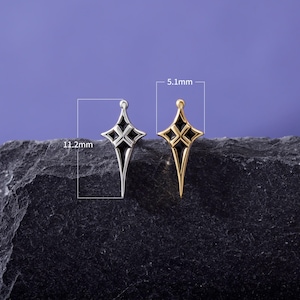 May include: Two star-shaped charms, one silver-toned and one gold-toned, each featuring black enamel inlay. The charms measure 11.2 mm in height and 5.1 mm in width, as indicated by the technical dimension lines overlaid on the image.