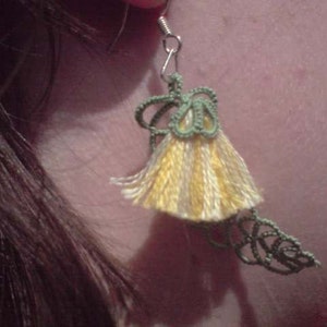 May include: A pair of earrings with a green and yellow tassel design. The tassel is made of yarn and has a delicate, feminine look.