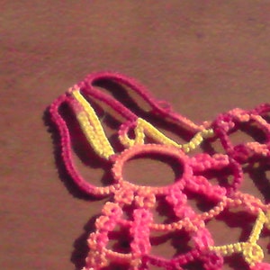 May include: A close-up of a crocheted lace doily in shades of pink and yellow. The doily is made of delicate, intricate stitches and has a circular shape.