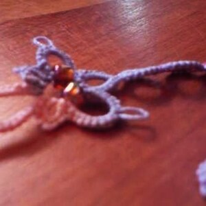 May include: A close-up of a purple and pink crocheted necklace with brown beads. The necklace is on a wooden surface.