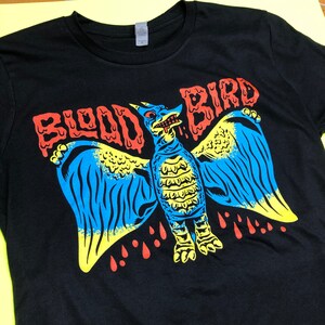 May include: Black t-shirt with a graphic print of a blue and yellow monster with red dripping blood. The text "BLOOD BIRD" is printed in red above the monster.