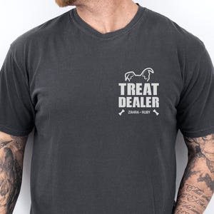 K&ouml;nnte beinhalten: Dunkelgraues V-Ausschnitt-T-Shirt mit dem wei&szlig;en Schriftzug "TREAT DEALER", einer Hunde-Silhouette und den Namen "ZAHRA - RUBY". Dieses l&auml;ssige T-Shirt ist aus weichem Stoff und eignet sich f&uuml;r den Alltag.