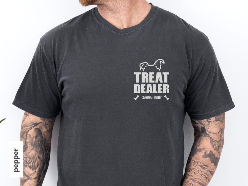 K&ouml;nnte beinhalten: Dunkelgraues V-Ausschnitt-T-Shirt mit dem wei&szlig;en Schriftzug "TREAT DEALER", einer Hunde-Silhouette und den Namen "ZAHRA - RUBY". Dieses l&auml;ssige T-Shirt ist aus weichem Stoff und eignet sich f&uuml;r den Alltag.