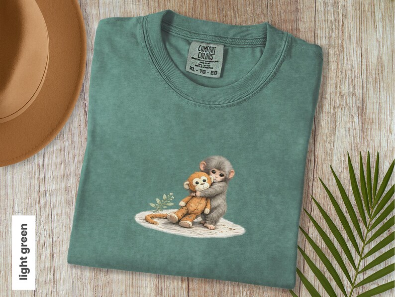 Monkey Punch Comfort Colors T-shirt, T-shirt met babyaapje dat een knuffel vasthoudt, cadeau voor dierenliefhebbers, virale meme van een verdrietig aapje, grafisch T-shirt voor mama en kind. Light Green
