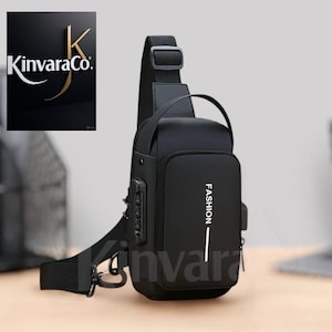 Peut inclure: Sac bandoulière noir avec le mot "FASHION" imprimé en blanc. Il est équipé d'un cadenas à combinaison, d'un port USB et d'une bandoulière. Le logo Kinvara Co. est visible en haut à gauche.